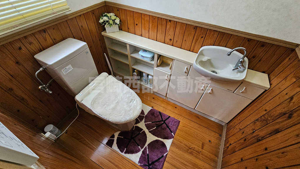 手洗い器付きの広々としたトイレ。木の腰壁が落ち着いた雰囲気を演出します。